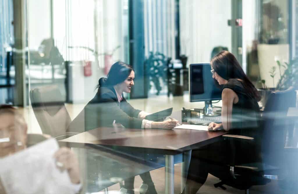 Mitarbeiter im Gespräch im modernen Büro mit Glaswänden und Computer.