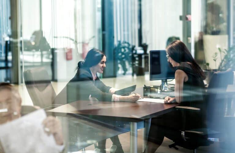 Mitarbeiter im Gespräch im modernen Büro mit Glaswänden und Computer.