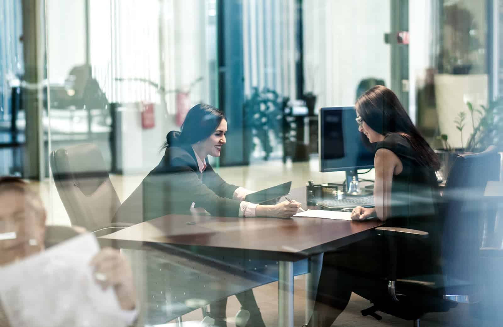 Mitarbeiter im Gespräch im modernen Büro mit Glaswänden und Computer.