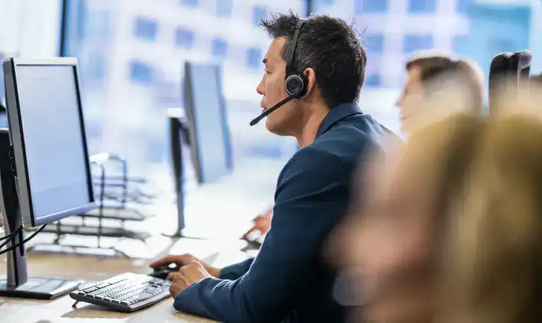 Mitarbeiter im Callcenter mit Headset arbeitet an Computer im Büro.