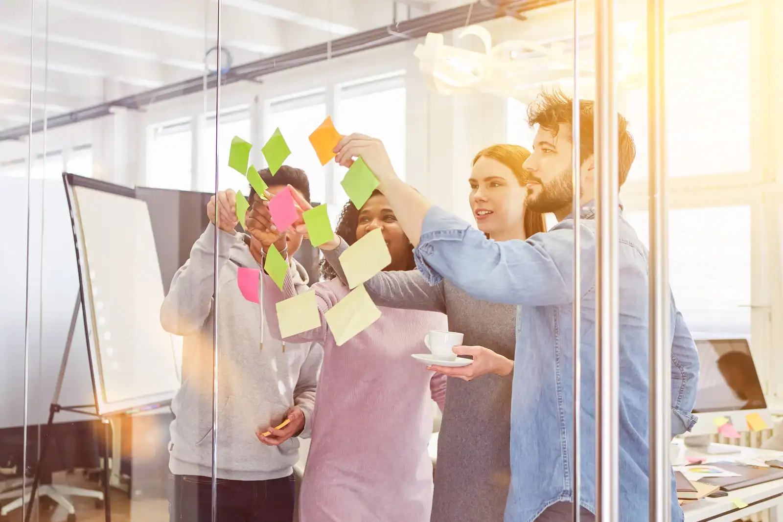 Drei Teammitglieder arbeiten gemeinsam an einer Glasscheibe mit bunten Post-its.