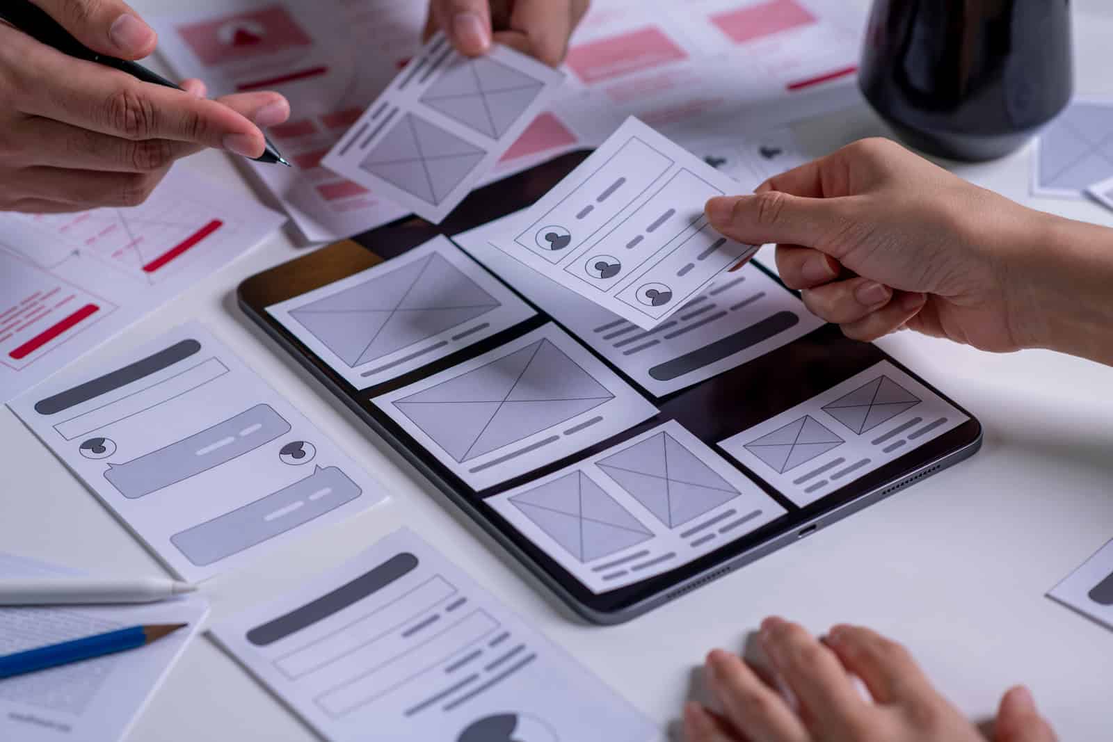 Zwei Personen arbeiten an einem Tablet mit Wireframes und Design-Entwürfen für mobile Apps.
