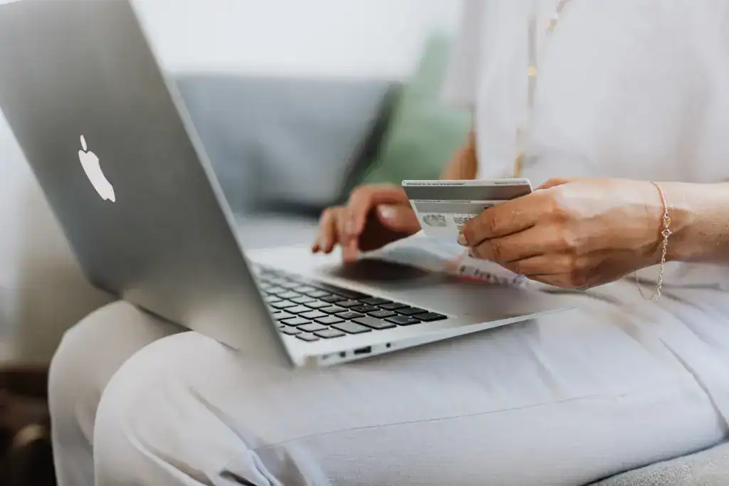 Person hält Kreditkarte vor einem offenen Laptop.